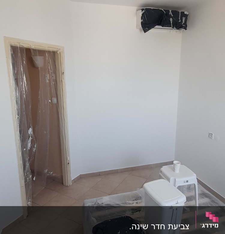 חדר עם כיסוי ניילון על מיטה, דלי וצבע.